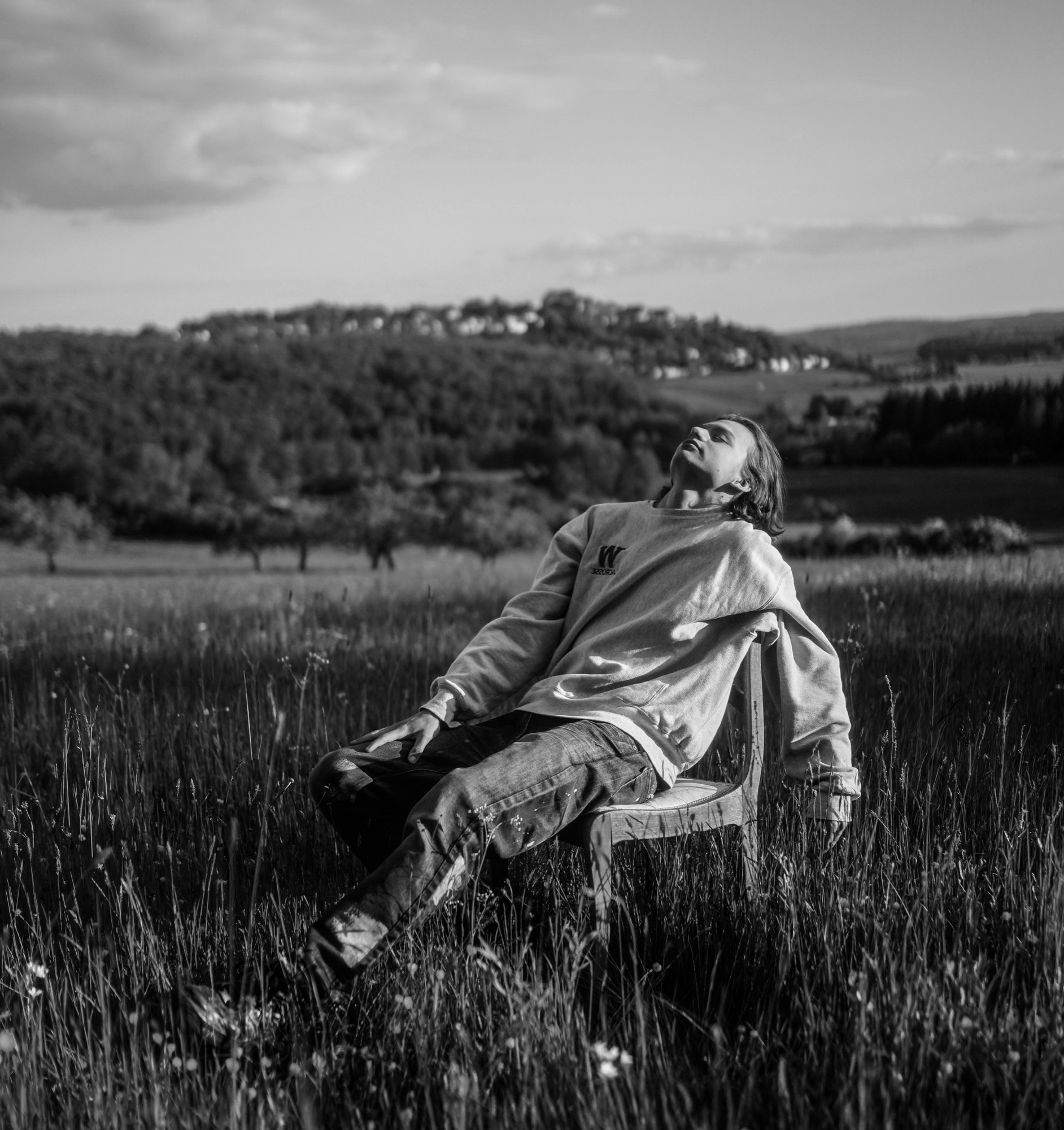 A man sitting back on a chair in a meadow, face to the sky